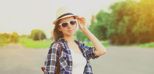 Portrait of young woman wearing summer straw hat, shirt and backpack on city street in summer park