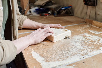 Close-up of unrecognizable joiner shaping wooden object on benchtop router table in woodworking...