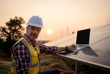 Portrait of engineer wearing yellow vest and white helmet using a computer laptop checking and maintenance of the solar panels, Sustainable energy concept