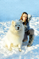 teenage girl plays with a dog of the Samoyed breed dog fluffy snow-white and big she plays outside in the snow hugging and having fun girl beautiful and young she is brown-haired.