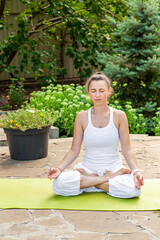 Young woman practices yoga in the garden, sitting in the Lotus position, hands folded in Jnana mudra and meditating