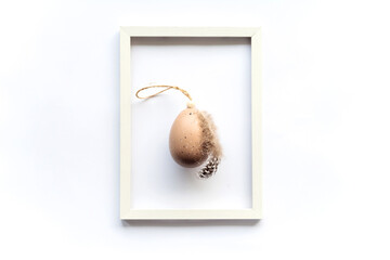 Easter natural egg with bird feather on white background with framed copy space for text. Minimal concept. View from above. Easter card, soft selective focus.