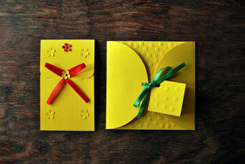 Yellow envelopes with colored ribbonson a wooden table made by hand. Flat lay, top view - Powered by Adobe