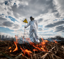 Firefighter ecologist extinguishing fire in field. Man in protective radiation suit and gas mask...
