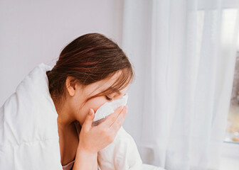 A cold girl blows her nose in a white rag on white background. Rhinitis snot runny nose stuffy nose. Allergy Preteen girl with handkerchief. medical concept