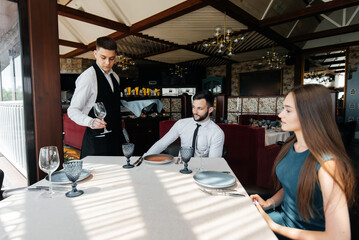 A stylish waiter serves a young couple of a man and a woman who came on a date to a gourmet restaurant. Customer service in the restaurant and catering establishments.
