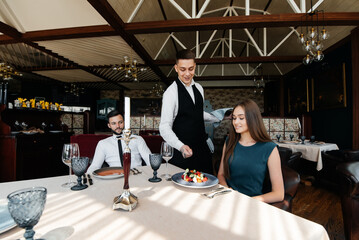 A stylish waiter serves a young couple of a man and a woman who came on a date to a gourmet restaurant. Customer service in the restaurant and catering establishments.