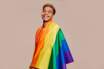 Portrait of happy smiling afro latin american young man with a gay pride rainbow flag at studio...