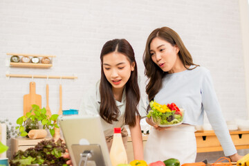 Two beautiful Asian friends in sportswear cook salads in the kitchen.