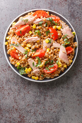 Boiled spelled with tuna, corn, tomatoes and herbs close-up in a plate on the table. vertical top view from above