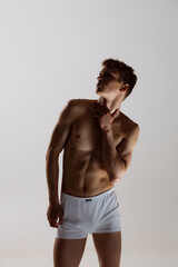 Fototapeta na wymiar Silhouette of young shirtless muscled man wearing white boxer-briefs standing isolated on gray background. Natural beauty of male body. Emotions, love, care