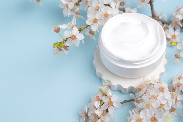 Obraz na płótnie Canvas Container with bodycare and skincare cream on a blue background with blooming cherry. Cosmetic facial skin care and spa. Natural treatment concept.