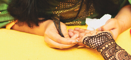 A female artist performing mehandi or henna design on female hand.