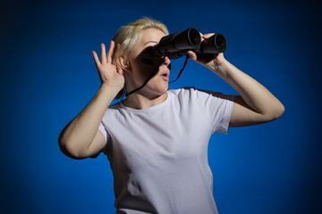 A blonde woman with a blue-yellow Ukrainian flag on her cheek looks through binoculars and...