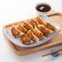 Pan-fried gyoza dumpling jiaozi in a plate with soy sauce on white table background.