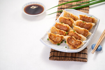 Pan-fried gyoza dumpling jiaozi in a plate with soy sauce on white table background.