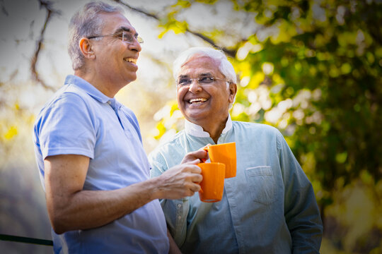Two old male friends having fun raising a toast with coffee cups at park