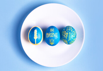 Easter eggs on white plate and painted with Ukrainian national colors, blue and yellow, and depicting Ukrainian national symbols: spikelet of wheat, trident, ornament