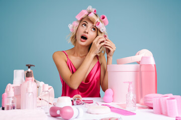 Young woman doing hairstyle with curlers while sitting at table
