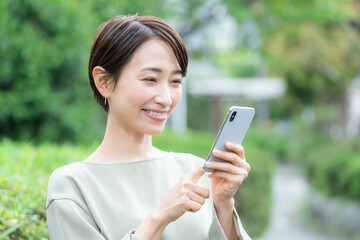 スマホを使うミドル女性（新緑・屋外）