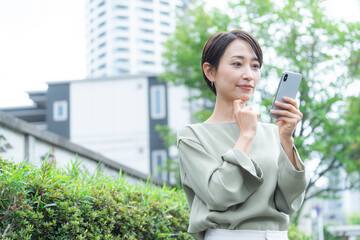 Fototapeta premium スマホを使うミドル女性（新緑・屋外）