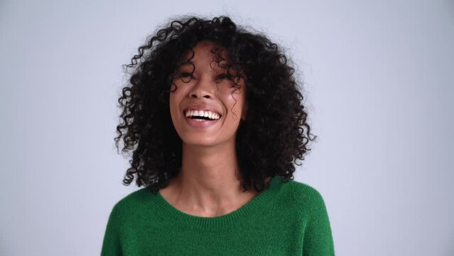 Positive curly-haired woman laughing at the camera in the grey studio
