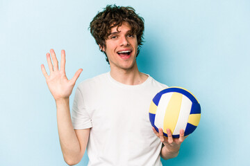 Young caucasian man playing volleyball isolated on blue background smiling cheerful showing number...