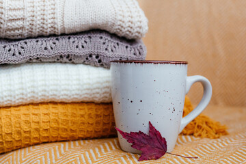 Fototapeta na wymiar Stack of soft warm plaids, a mug and an autumn leaf close-up.