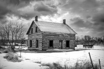 An old black and white abandoned farmhouse in winter on a farm yard in rural Ontario, Canada