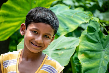 The portrait of a beautiful serene Indian child in the background of a dark green forest and he is looking at the camera in a casual dress and smiling beautifully