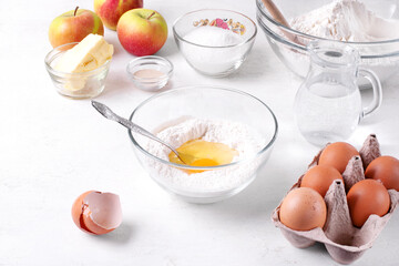 Making sourdough for yeast dough. Mixing flour, dry yeast, eggs, sugar and water in the glass bowl. Preparing buns or pie with apple filling on the white table. Step by step recipe. Step 2