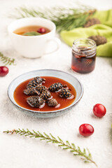 Pine cone jam with herbal tea on gray concrete, side view, selective focus.