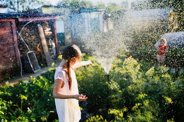 Hot summer and garden. Children bathe under the spray of a garden watering system. Children dance...