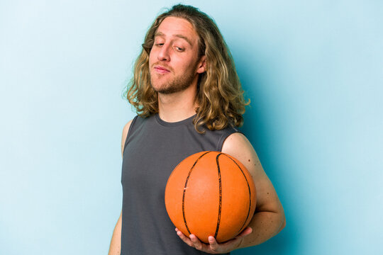 Young caucasian man playing basketball isolated on blue background looks aside smiling, cheerful and pleasant.