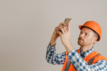 White man worker wearing helmet and vest using mobile phone