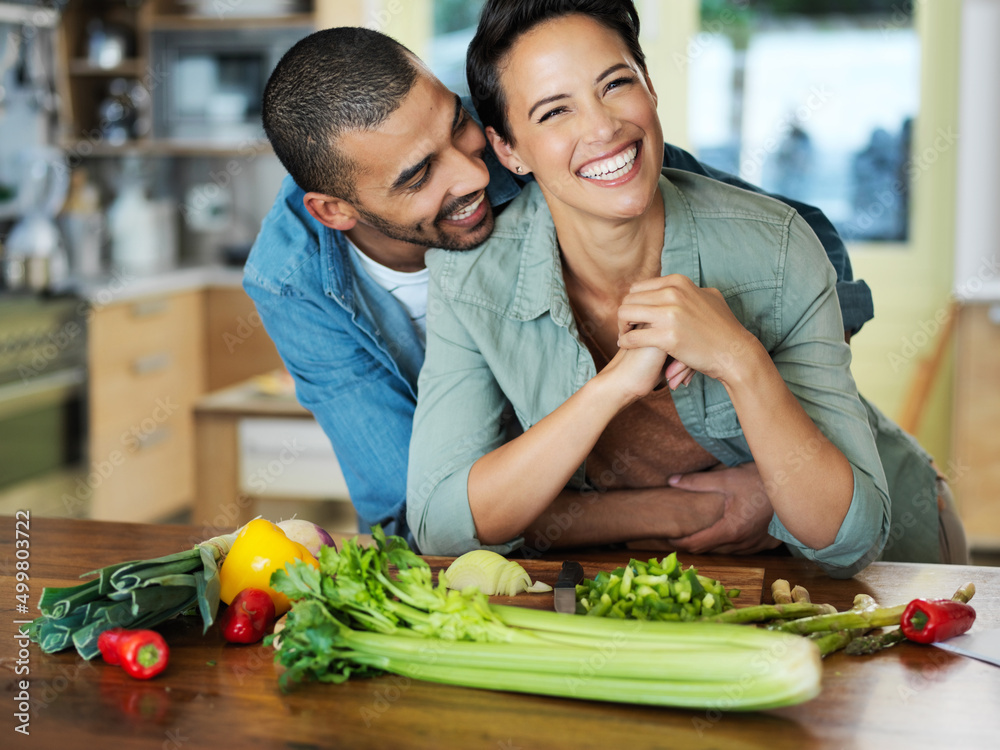 Wall mural Putting love in their meal. Portrait of an affectionate young couple preparing a meal together in their kitchen.