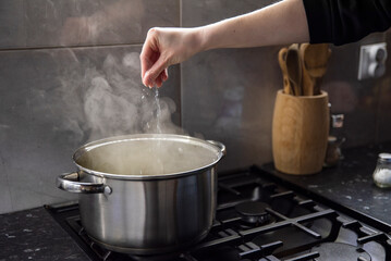 Fototapeta na wymiar Kobieta soli parujące danie w garnku.