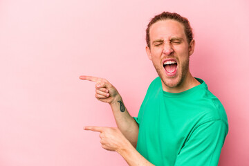 Young caucasian man isolated on pink background excited pointing with forefingers away.