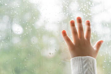 partial view of kid touching window glass with raindrops.