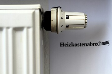 Thermostat an einem Heizkörper. Rechts ein Blatt Papier mit der Aufschrift 