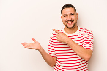 Young hispanic man isolated on white background excited holding a copy space on palm.