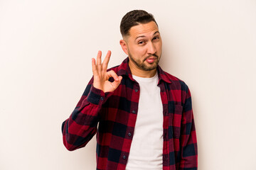 Young hispanic man isolated on white background winks an eye and holds an okay gesture with hand.
