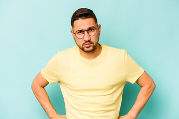 Young hispanic man isolated on blue background sad, serious face, feeling miserable and displeased.