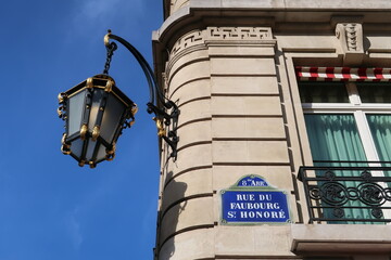 Plaque de rue de la prestigieuse rue du Faubourg Saint Honoré dans la ville de Paris, adresse du palais de l’Élysée, d'ambassades et de boutiques de luxe, avec un réverbère ancien (France) - obrazy, fototapety, plakaty