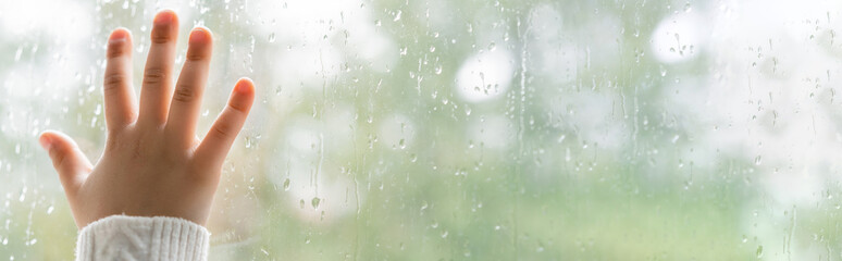 partial view of child touching wet window glass, banner.