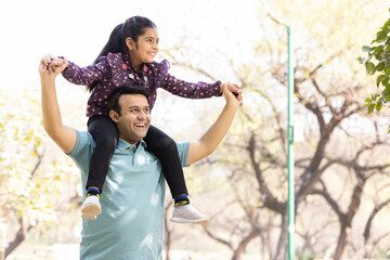 Happy man with daughter sitting on shoulders having fun at park