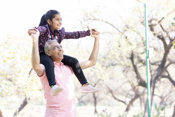 Senior man with granddaughter sitting on shoulders having fun at park