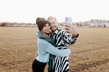 Couple taking a selfie photo with mobile phone in countryside at sunset