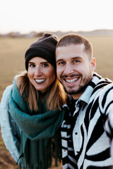 Couple taking a selfie photo in countryside at sunset. Focus on man.