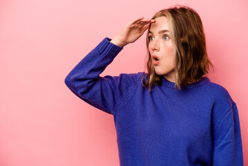 Young caucasian woman isolated on pink background looking far away keeping hand on forehead.